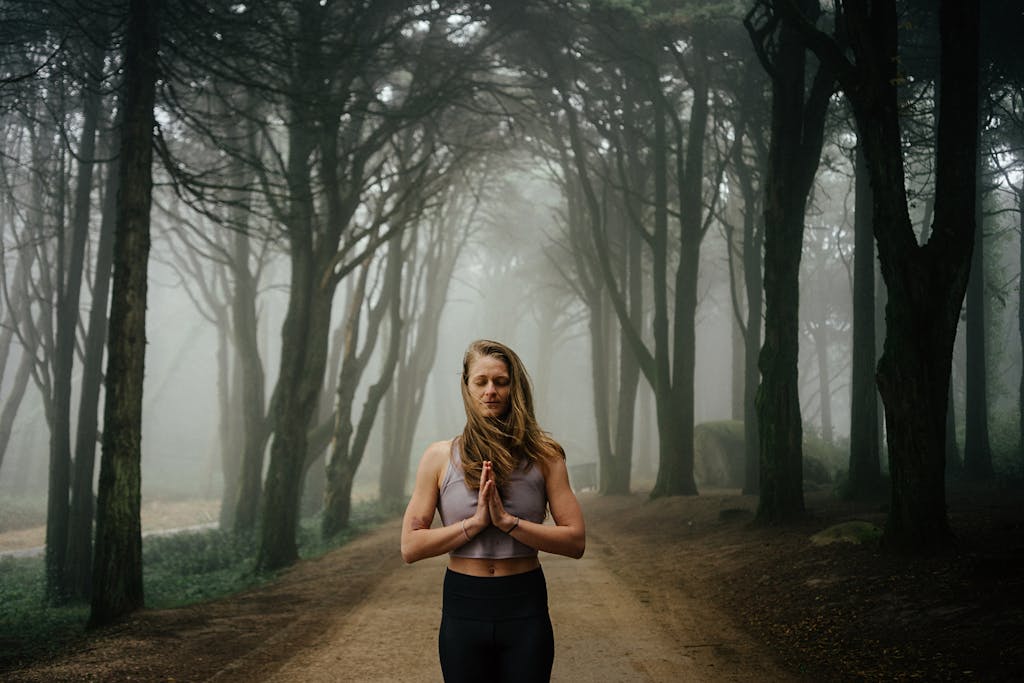 Woman meditating in tranquil forest setting with mist and trees.