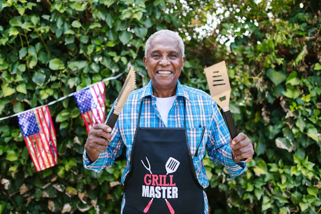 Happy senior man wearing grill master apron at outdoor barbecue with American flags.