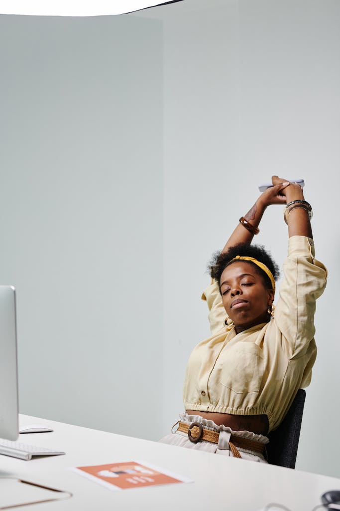 African American woman stretching with eyes closed at her office desk, feeling relaxed.